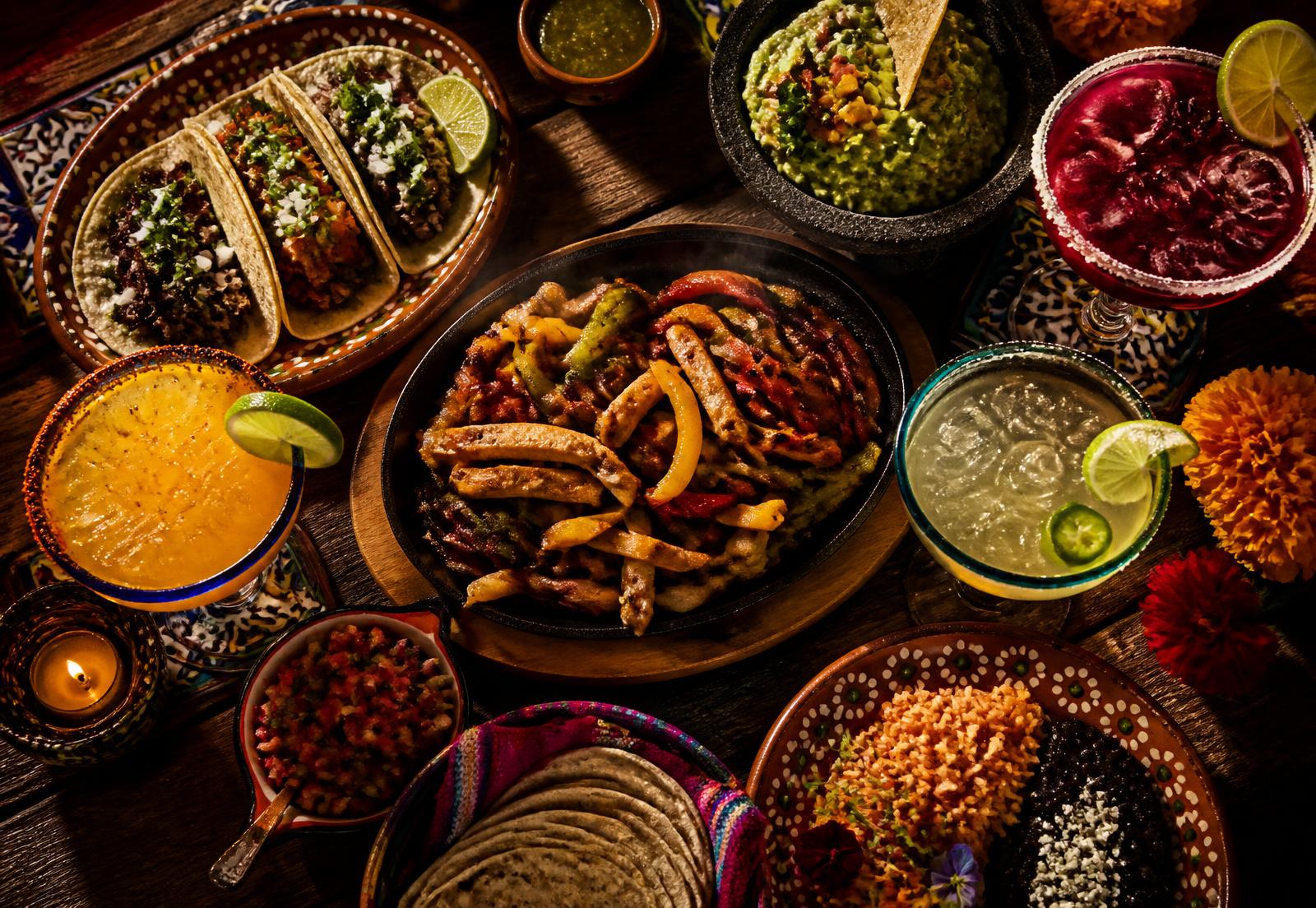 Table full of Mexican dishes: fajitas, street tacos, guacamole and margaritas
